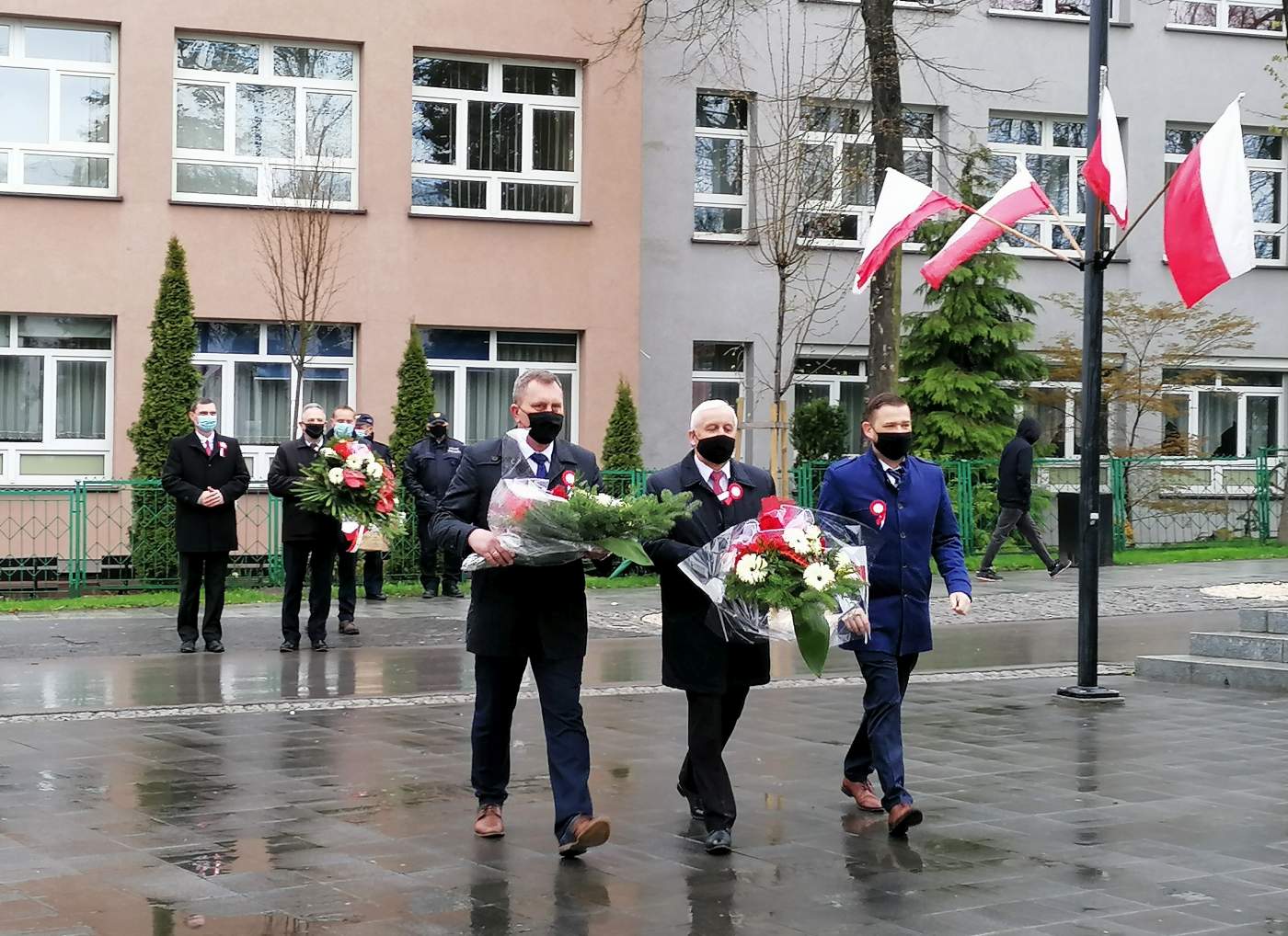 Zdjęcie przedstawia Przewodniczącego Rady Miejskiej Roberta Burchana niosącego wiązankę, Burmistrza Miasta i Gminy Busko-Zdrój Waldemara Sikorę niosącego wiązankę oraz Z-cę Burmistrza Miasta i Gminy Busko-Zdrój Michała Marońskiego.