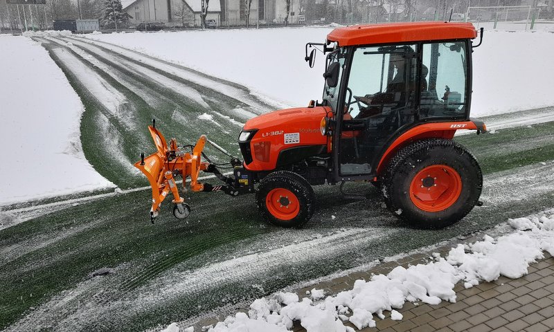 Zdjęcie przedstawia ciągnik w trakcie odsnieżania 