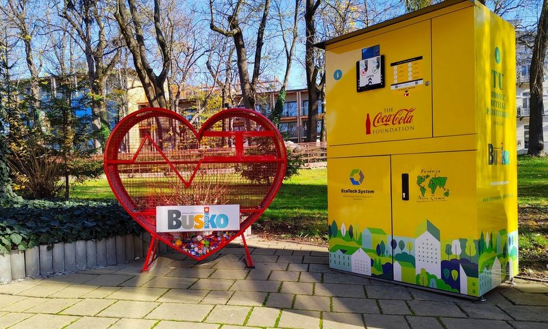 zdjęcie przedstawia pojemnik na nakrętki w kształcie serca stojący obok automatu do zbiórki butelek