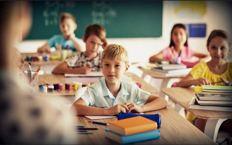 zdjęcie przedstawia dzieci siedzące w szkolnych ławkach