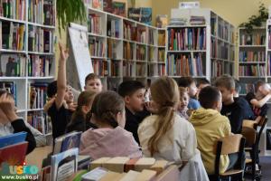Dzieci siedzą przy stoliku, w tle regały z książkami