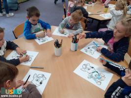 Dzieci siedzą przy stoliku i kolorują malowanki