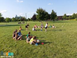 Zdjęcie przedstawia grupę uczestników w trakcie zabaw ruchowych na terenie Parku Zdrojowego