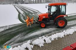 Zdjęcie przedstawia ciągnik w trakcie odsnieżania 