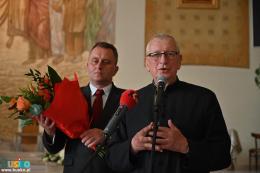 Przemawia nagrodzony ksiądz Marek Podyma, z tyłu przewodniczący Burchan trzyma bukiet kwiatów