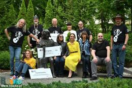 Muzycy i organizatorzy pozuja do zdjęcia przy ławeczce Wojtka Belona