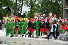 Na zdjęciu dzieci przebrane w kwieciste stroje stoją obok fontenny