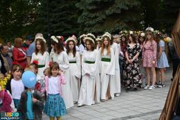 Młodzież i dzieci w kwiecistych strojach stojące na placu przy fontannie