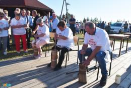 Troje siedzących zawodników ubija masło w maselniczkach, w tle publiczność