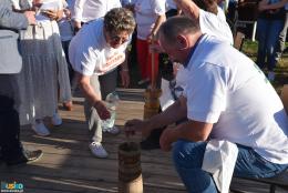 Mężczyzna ubijający masło w maselnicy, kobieta z butelką wody, w tle publiczność