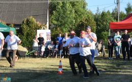 Trwa konkurencja powożenia zaprzęgiem. Dwóch biegnących mężczyzn z zawiązanymi oczami, za nimi kolejny odgrywający rolę woźnicy 