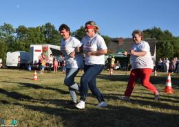 Trwa konkurencja powożenia zaprzęgiem. Dwie biegnące kobiety z zawiązanymi oczami, za nimi kolejna odgrywająca rolę woźnicy 