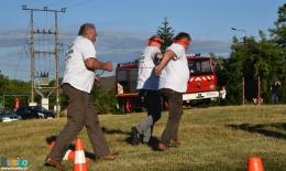 Trwa konkurencja powożenia zaprzęgiem. Dwóch biegnących mężczyzn z zawiązanymi oczami, za nimi kolejny odgrywający rolę woźnicy 