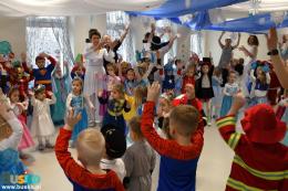Przedszkolaki w przebraniach karnawałowych tańczą w udekorowanej sali