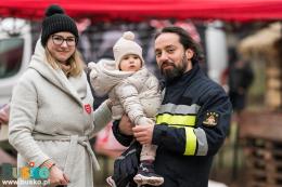Osoby pozujące do zdjęcia - kobieta, mężczyzna w stroju strażackim z dzieckiem na ręku