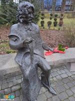 Rzeźba - ławeczka Wojtka Belona przy al. Mickiewicza, obok rzeźby na ławce leży czerwony kwiat ze wstążką 