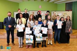 Uczestnicy spotkania pozujący do zdjęcia na tle prac konkursowych