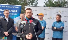 Przemawia Z-ca Burmistrza Michał Maroński, w tle uczestnicy biegu