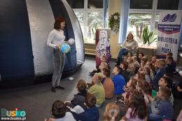 Kobieta prezentuje modele planet dzieciom, obok kopuła planetarium